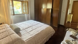 Camera da letto con un letto grande, un armadio, un tavolo con oggetti e una finestra con tende.