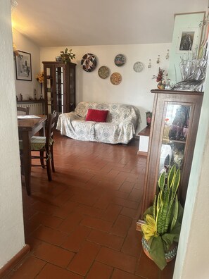 A living room with a sofa, a dining table, and chairs. There are decorative plates on the wall and a potted plant on the floor.