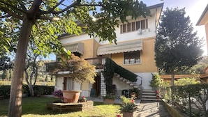 Una casa a due piani con un vialetto in pietra che conduce all'ingresso, circondata da piante in vaso e un prato ben curato.
