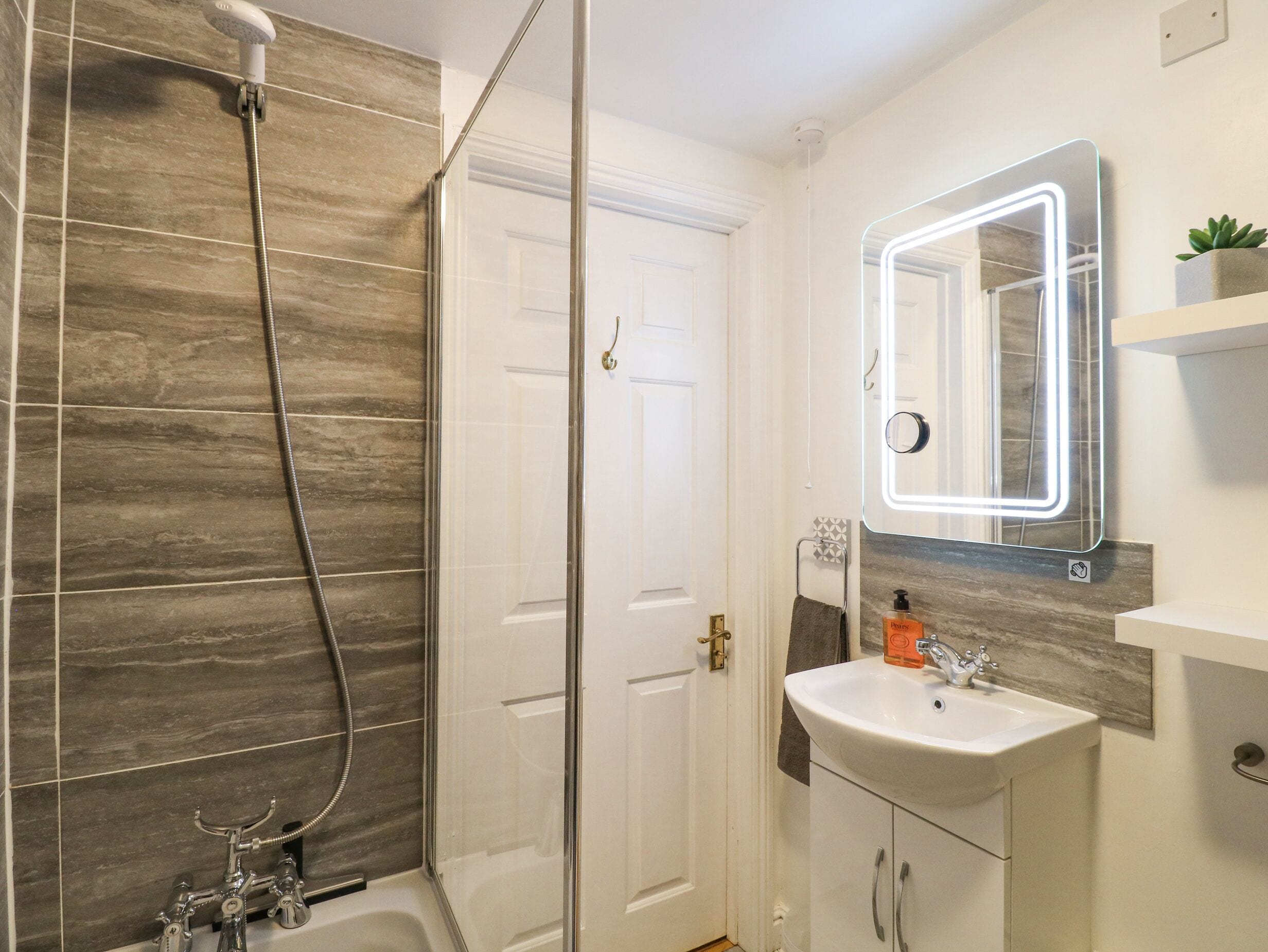 Een badkamer met een douche, wastafel en spiegel.