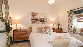 A neatly arranged bedroom with a large bed, two bedside tables with lamps, a wall-mounted mirror, and a cityscape painting.