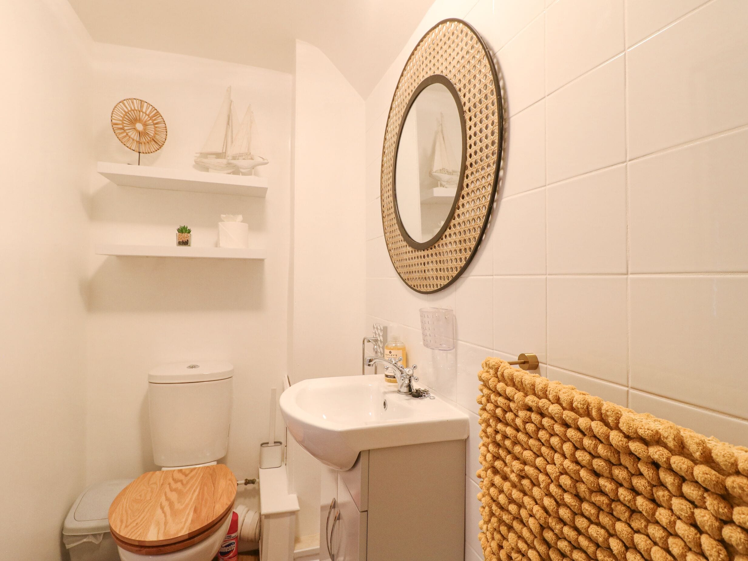 A bathroom with a toilet, sink, and mirror. There are shelves above the toilet and a towel rack to the right.