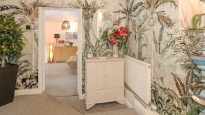 Un pasillo con papel tapiz tropical, un mueble blanco y una puerta que da a una zona de cocina.