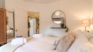 Un dormitorio con una cama grande, un espejo redondo, una lámpara de noche y una puerta que da a otra habitación.