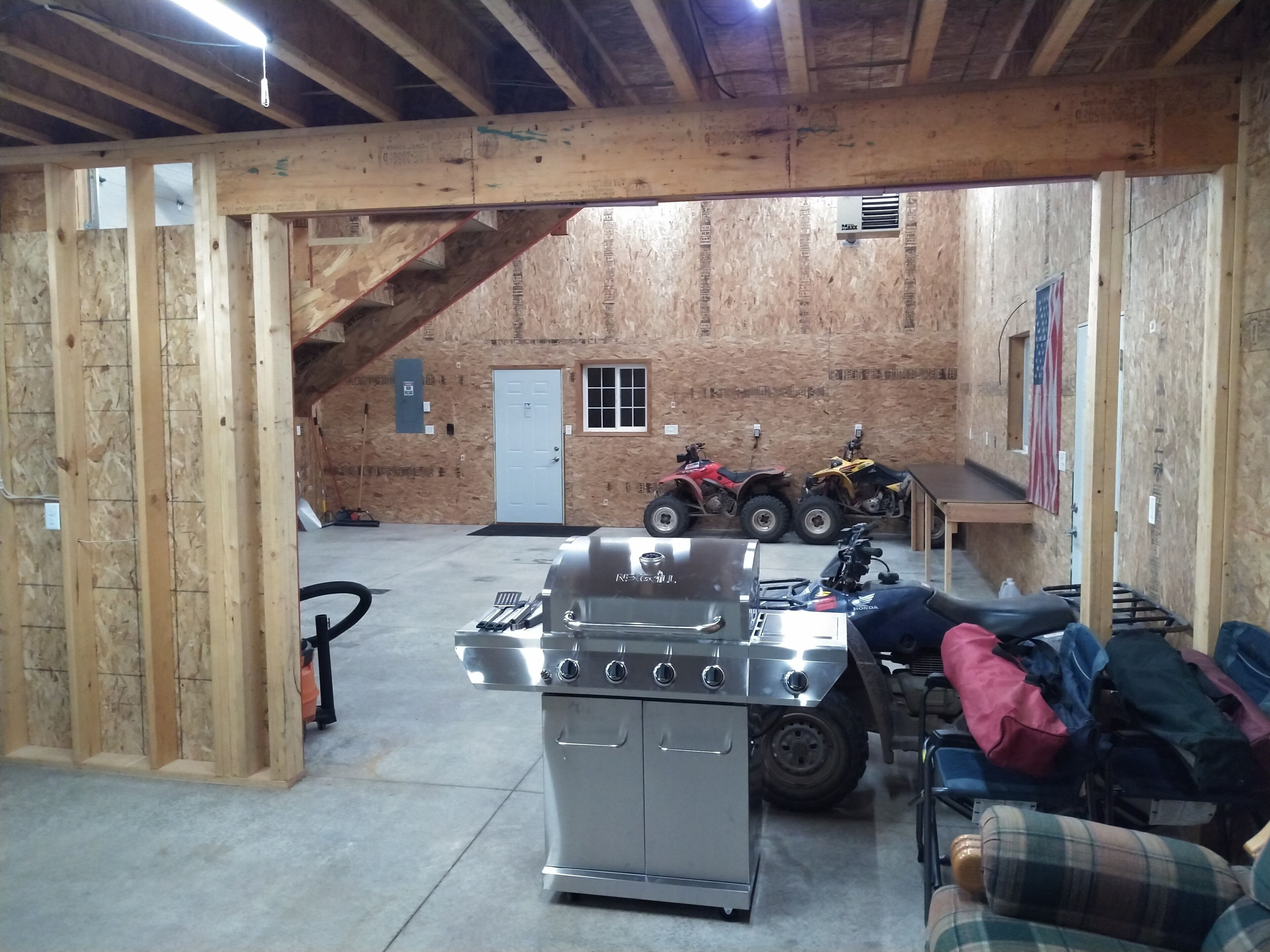 Un garage con interni in legno, un barbecue, due ATV e una porta che dà su un'altra stanza.