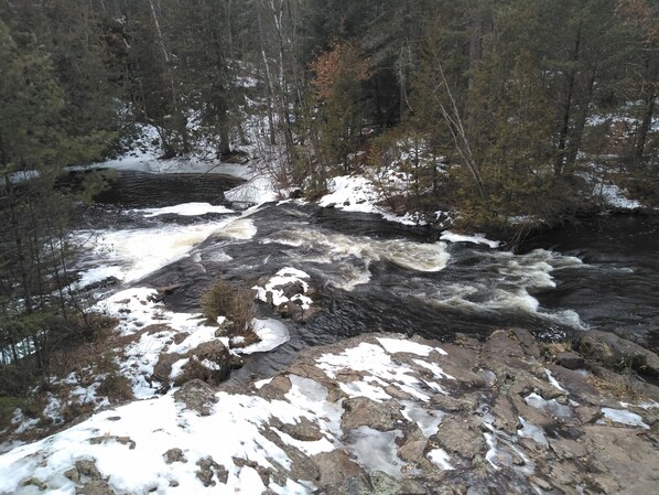 A river flowing through a forested area with snow patches on rocks and trees.