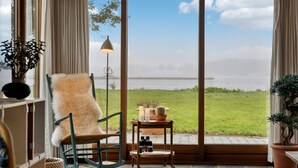 Une pièce avec vue sur un lac, un fauteuil à bascule, une petite table avec des bougies et une lampe.