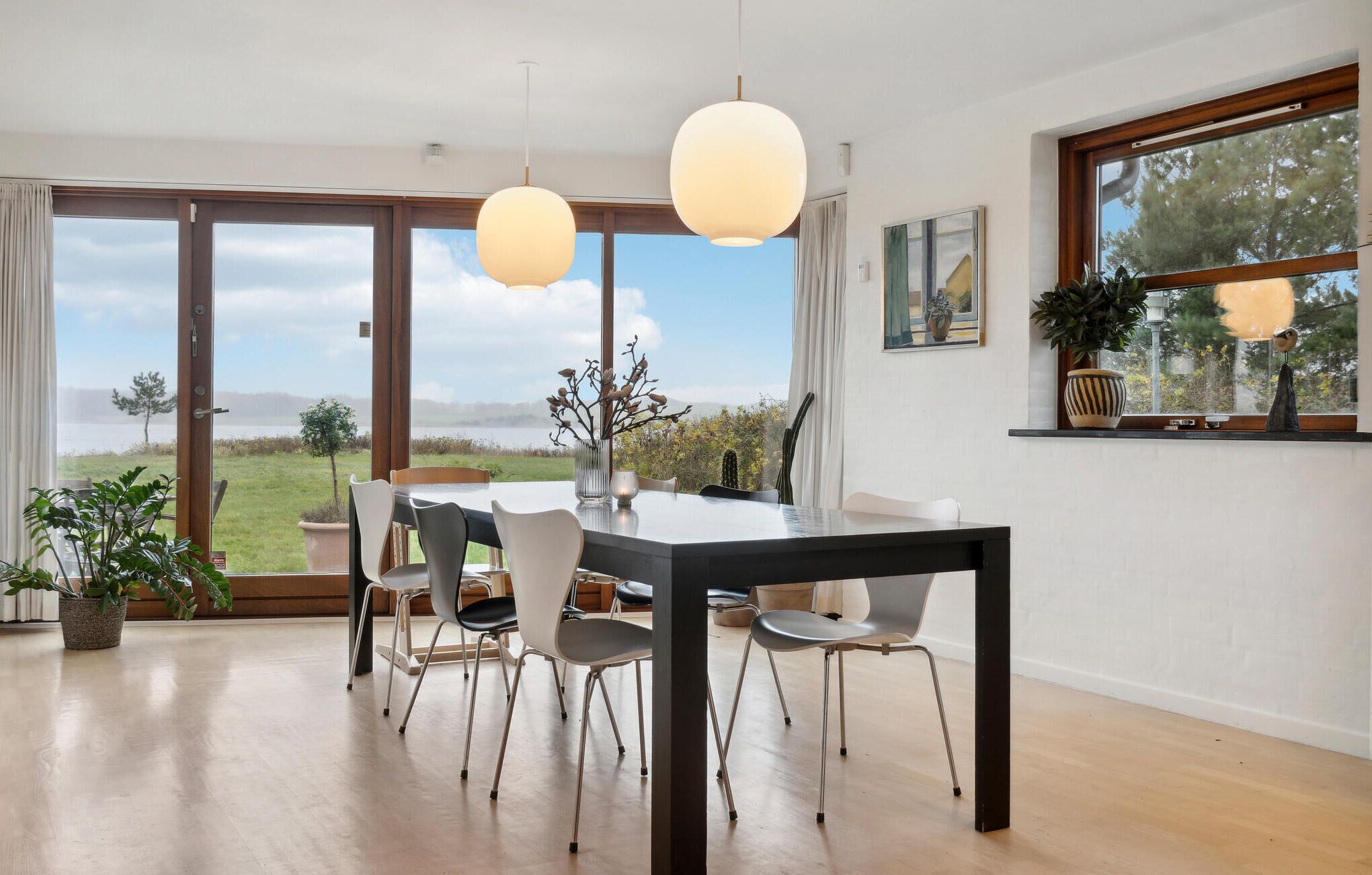 A dining area with a table and chairs, large windows with a view of the outdoors, and hanging pendant lights.