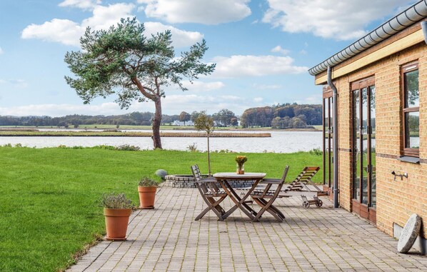Une terrasse avec une table et des chaises, un bâtiment en briques et une vue sur un lac.