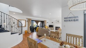 Ein großzügiger Wohnbereich mit einer geschwungenen Treppe, einem mit Kerze gedeckten Esstisch und einem Schild mit der Aufschrift 'BEACH HOUSE RULES RELAX RELAX'.