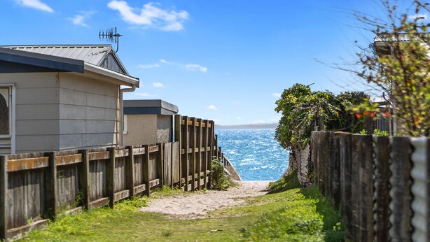 Ein Küsteneigentum mit Holzzaun, einem Weg zum Strand und einem Haus mit Metalldach und Satellitenschüssel.