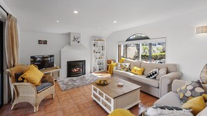 Ein Wohnzimmer mit Kamin, Sofa und Sesseln, inklusive Fernseher und Bücherregal.