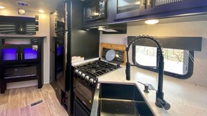 A compact kitchen with a gas stove, a microwave, and a refrigerator. - 4 units includes two cottages and two trailers with king and queen beds, kitchens, and dining areas. (Talent)