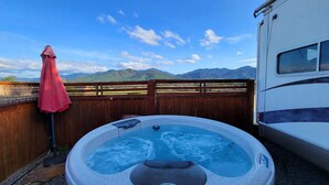 A hot tub with a view of mountains, a wooden fence, and a red umbrella. - 2 separate RV’s with queen-sized beds, dining area, and full kitchen. (Talent)