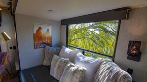 Ein modernes Zimmer mit einem großen Fenster, einem Sofa mit vielen Kissen, einem Poster an der Wand und einer Lampe.