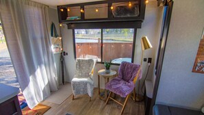 Ein gemütliches Zimmer mit zwei Sesseln, einem kleinen Tisch mit Pflanze und einem Fenster mit Blick ins Freie.