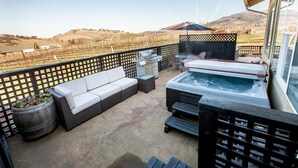 Une terrasse dotée d’un jacuzzi, d’un espace salon extérieur et offrant une vue sur un vignoble.