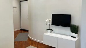 A modern hallway with a flat-screen TV mounted on a white console, a small potted plant, and a gray rug on the wooden floor. - CasaMia tra Navigli e Università (Milano)