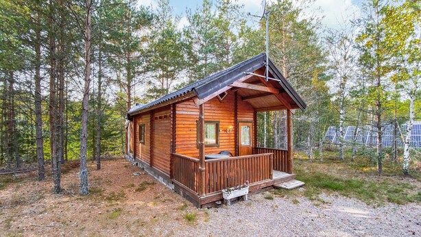 Une cabane en bois avec un porche, entourée d’arbres.