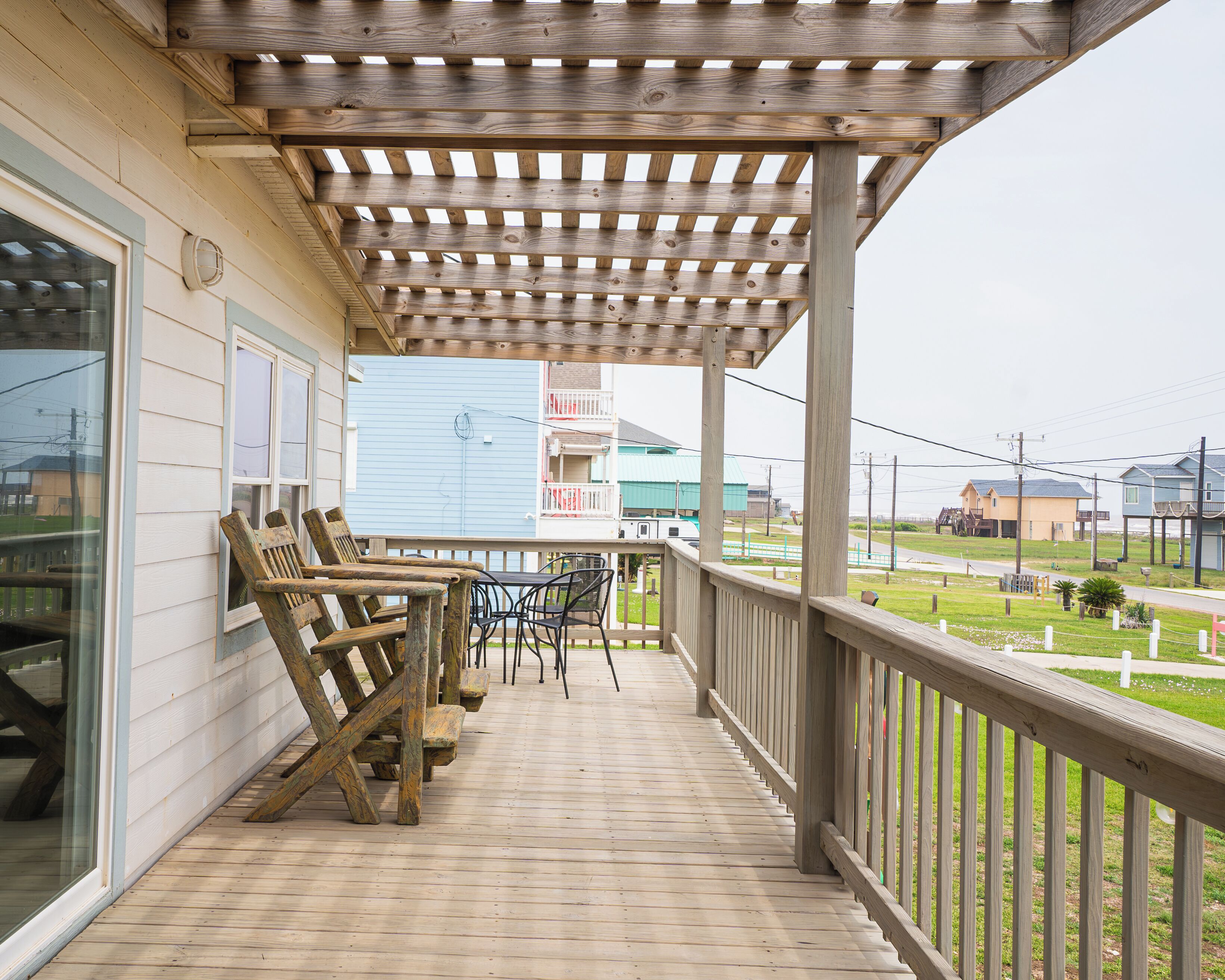 A wooden deck with a pergola, outdoor seating, and a view of a residential area.