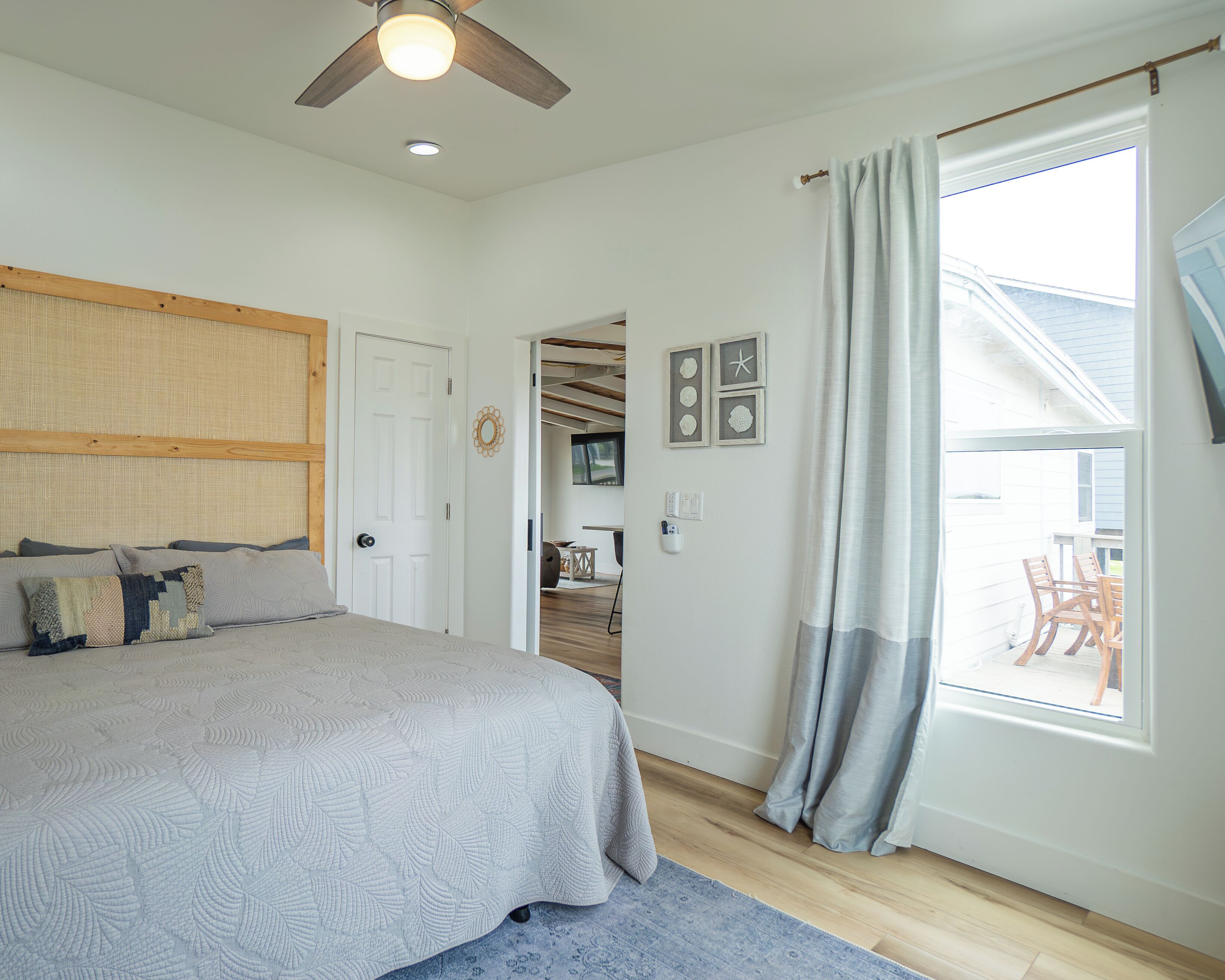 A bedroom with a bed, a ceiling fan, a window with curtains, and a view of the outside.
