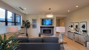 Een moderne woonkamer met een open haard, een grote televisie erboven en een bank.