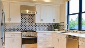 Een moderne keuken met witte kastjes, een roestvrijstalen fornuis en een raam met uitzicht op de omgeving.