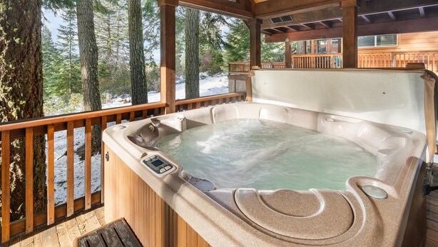 A wooden deck with a hot tub, large windows, and a view of trees.