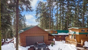 A cabin with a garage, surrounded by tall trees and snow.