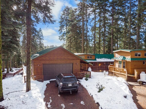 A cabin with a garage, surrounded by tall trees and snow.