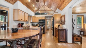 A spacious kitchen with wooden cabinets, a dining table, and a high ceiling with exposed beams.