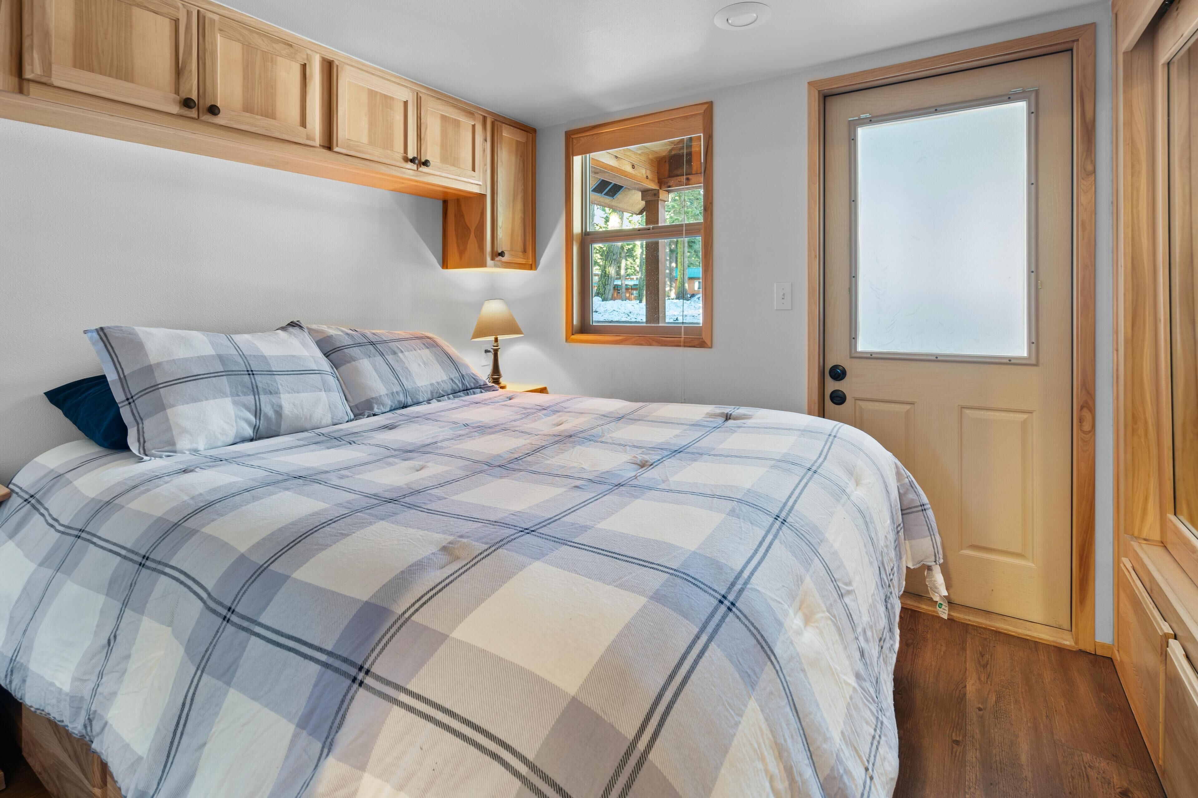 Une chambre à coucher avec une couvre-lit à carreaux, des armoires en bois, une fenêtre donnant sur un beau paysage et une porte.