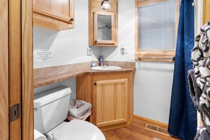 A compact bathroom with a toilet, sink, and mirror. A sign instructs not to flush any products other than toilet paper.