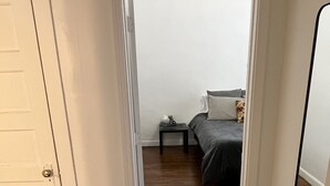 Un couloir menant à une chambre à coucher, où se trouvent un lit, une table de chevet et une porte.