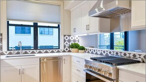 Una cocina moderna con armarios blancos, un lavavajillas de acero inoxidable, un horno empotrado y una ventana con vistas al exterior.