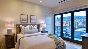 Un dormitorio con una cama grande, dos lámparas de noche, una mesita de noche y vistas a un balcón con mobiliario exterior.