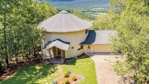 A single-story house with a circular section and a gabled roof, surrounded by a well-maintained lawn and trees. - Breathtaking mountain views-4king en suites, bunk rm, sauna, air hockey,MANCAVE! (Hot Springs Village)