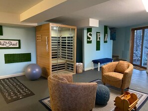 Ein Zimmer mit einem Holzschrank, einer blauen Bank, einem braunen Sessel, einem blauen Fitnessball und einem Holzregal.