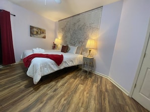 Une chambre à coucher avec un lit, deux lampes de chevet, un plaid rouge et une grande carte du monde accrochée au mur.