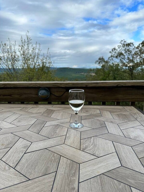 Una copa de vino blanco sobre una mesa de madera con un diseño geométrico, con vistas a un paisaje escénico con árboles y colinas.