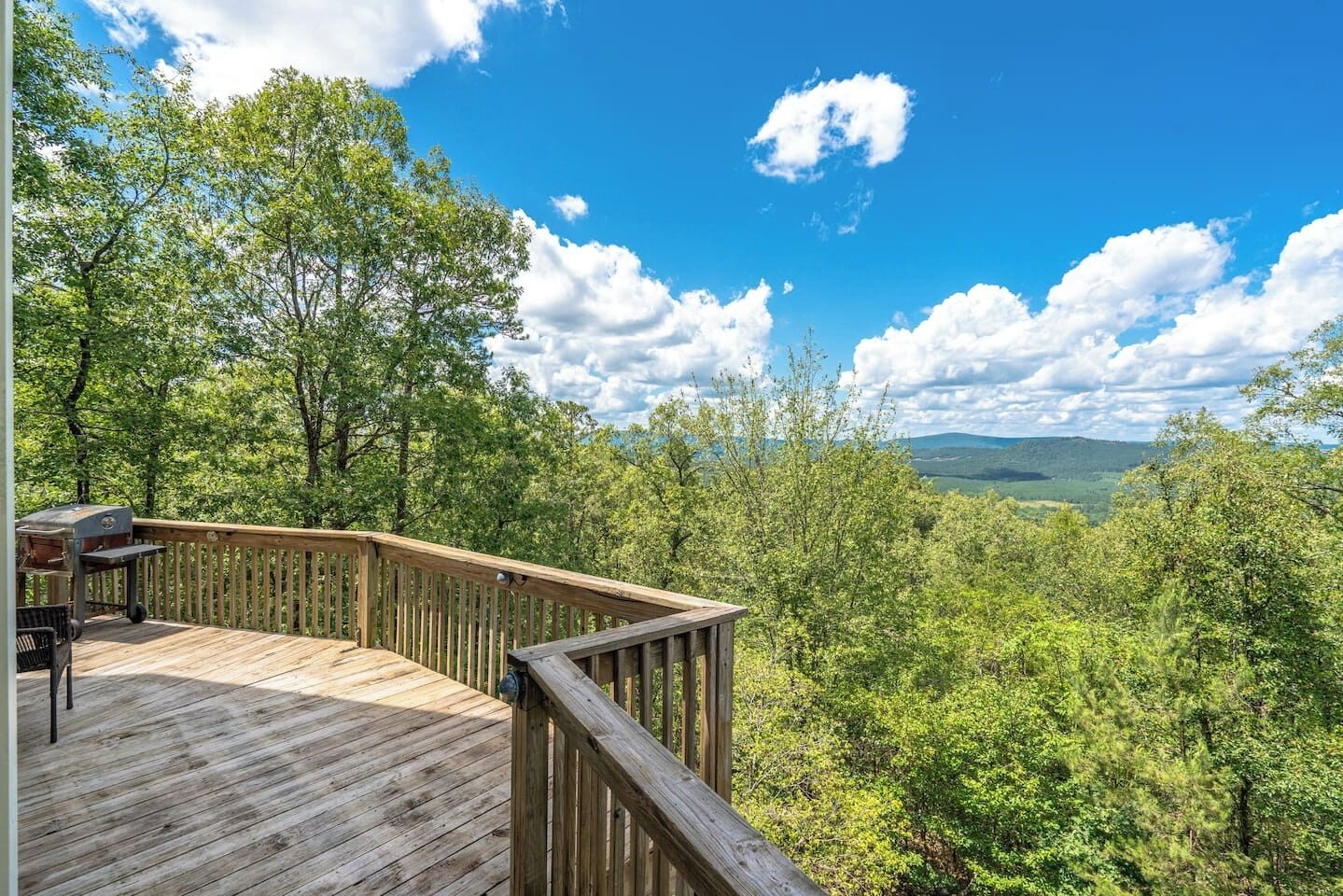 Une terrasse en bois offrant une vue sur une forêt et des collines lointaines.
