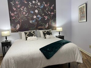 Une chambre à coucher avec un grand lit, deux tables de chevet avec des lampes, un tableau mural et un tableau encadré.