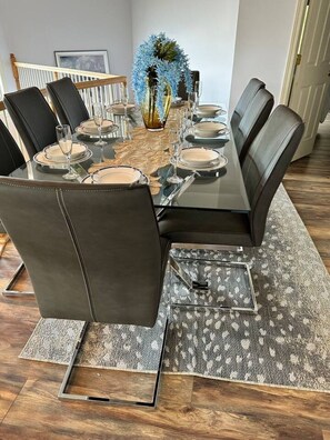 Mesa de comedor para seis personas con cubierta de vidrio, rodeada de sillas de cuero.