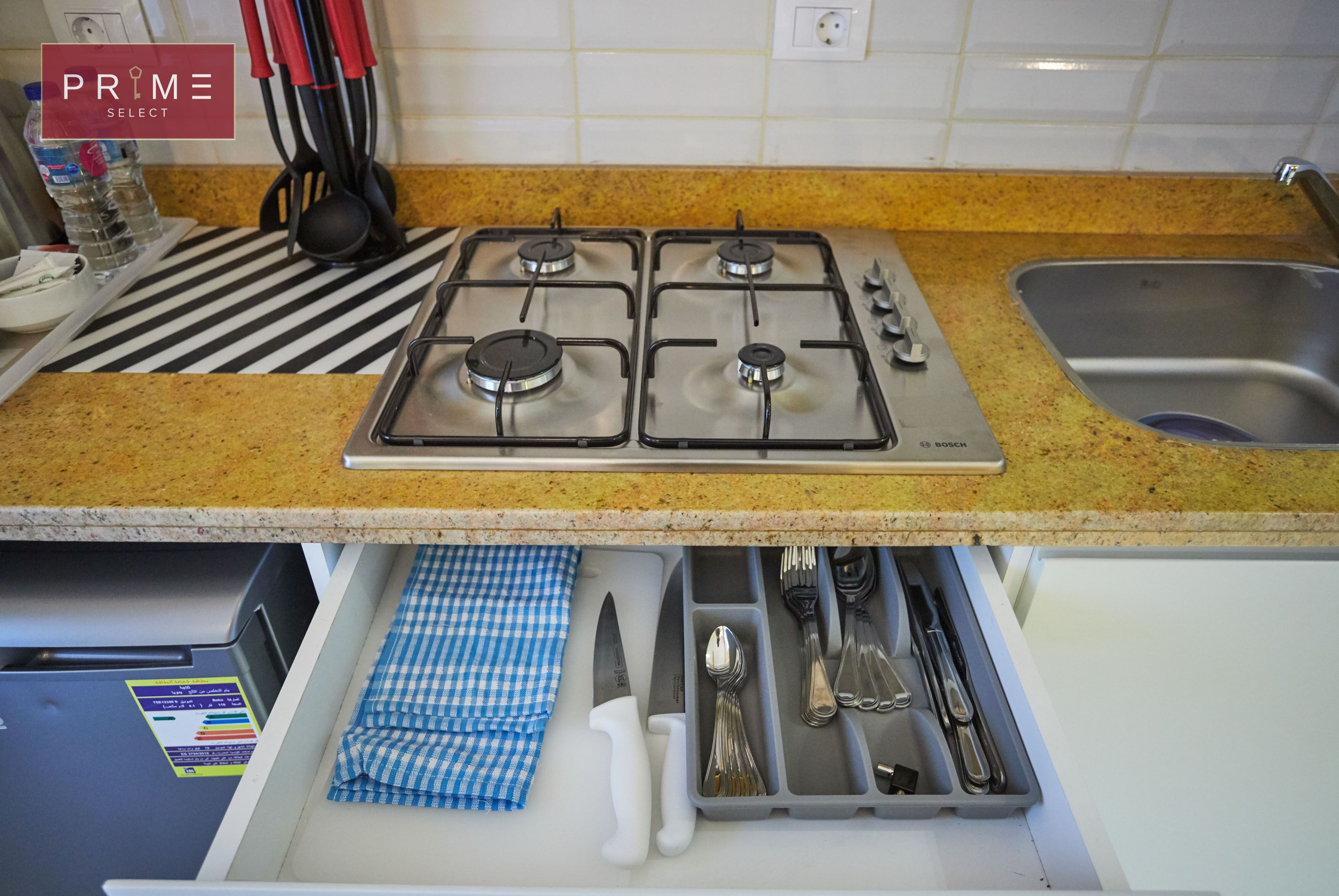A kitchen with a gas stove, stainless steel sink, and a drawer organizer with utensils.