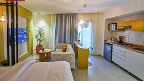 A modern hotel room with a bed, a sofa, a small desk, a kitchen area, and a TV mounted on the wall. - Prime Select Kattameya Bavaria (Cairo)