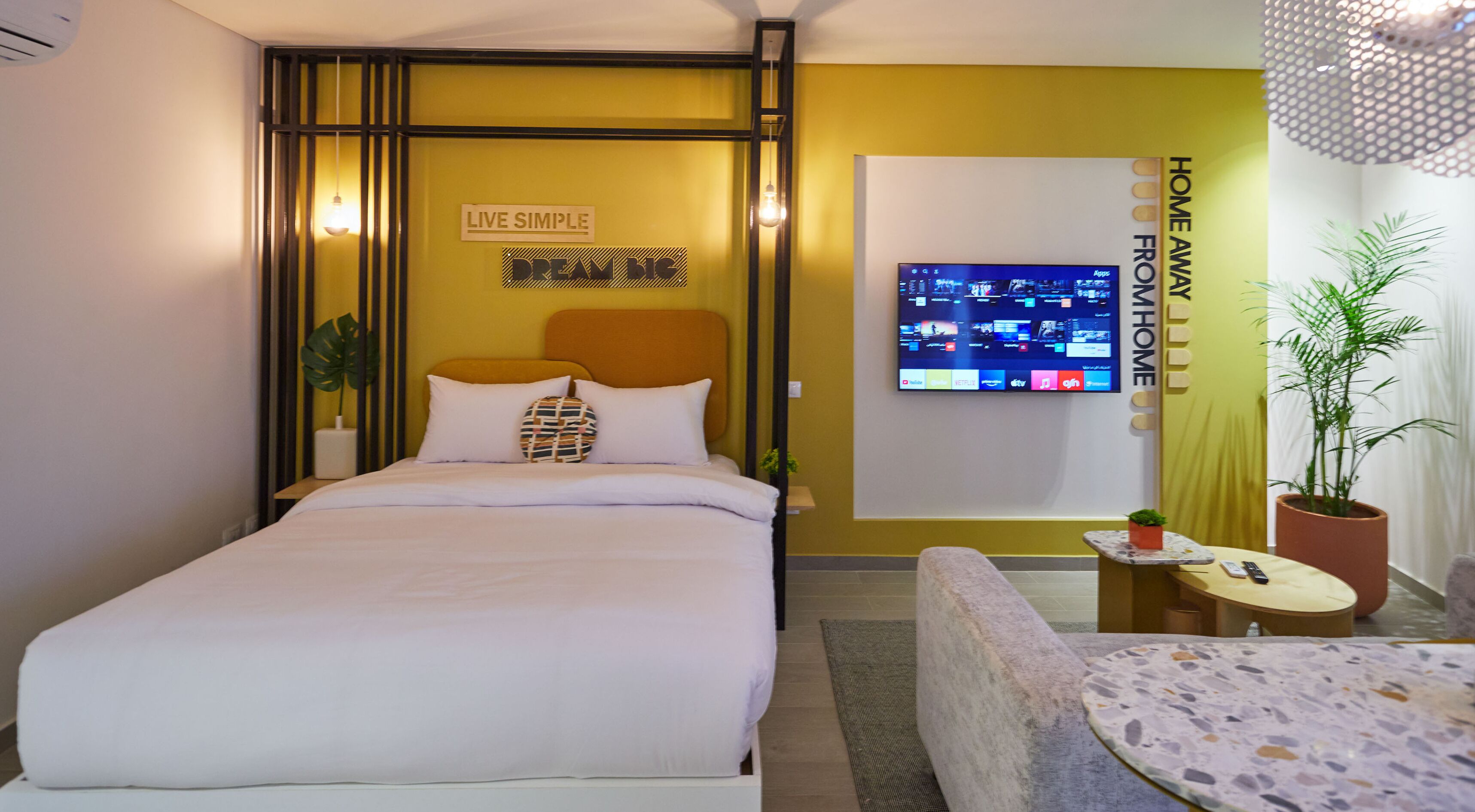Ein modernes Schlafzimmer mit einem Bett, einem an der Wand befestigten Fernseher und einem kleinen Tisch mit einer Pflanze.