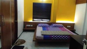 Quarto com cama, mesas de cabeceira, janela com persianas e porta.