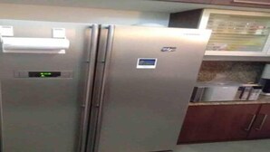 Uma geladeira de aço inoxidável com visor digital, micro-ondas e bancada de madeira em uma cozinha.