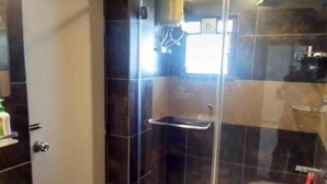 Casa de banho com cabine de duche em vidro, lavatório branco e uma pequena estante com artigos de higiene pessoal.