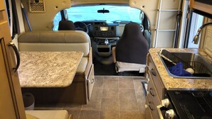 A compact RV interior with a kitchenette, a dining area, and a sleeping berth. - Road Surfer-- Resort-Style RV Stay Near The Strip (Las Vegas)
